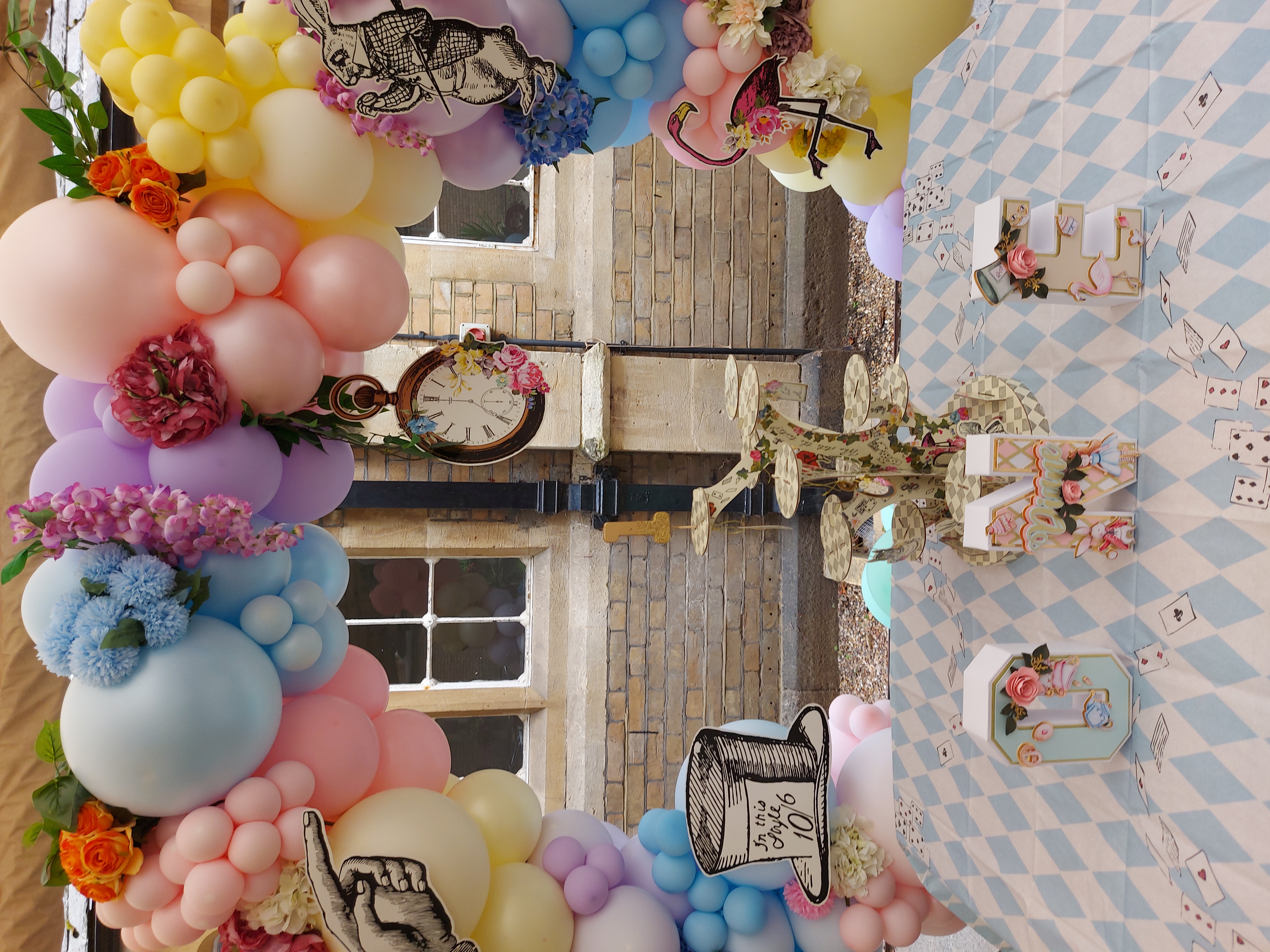 A balloon arch surrounds a tea table decorated with an Alice in Wonderland theme