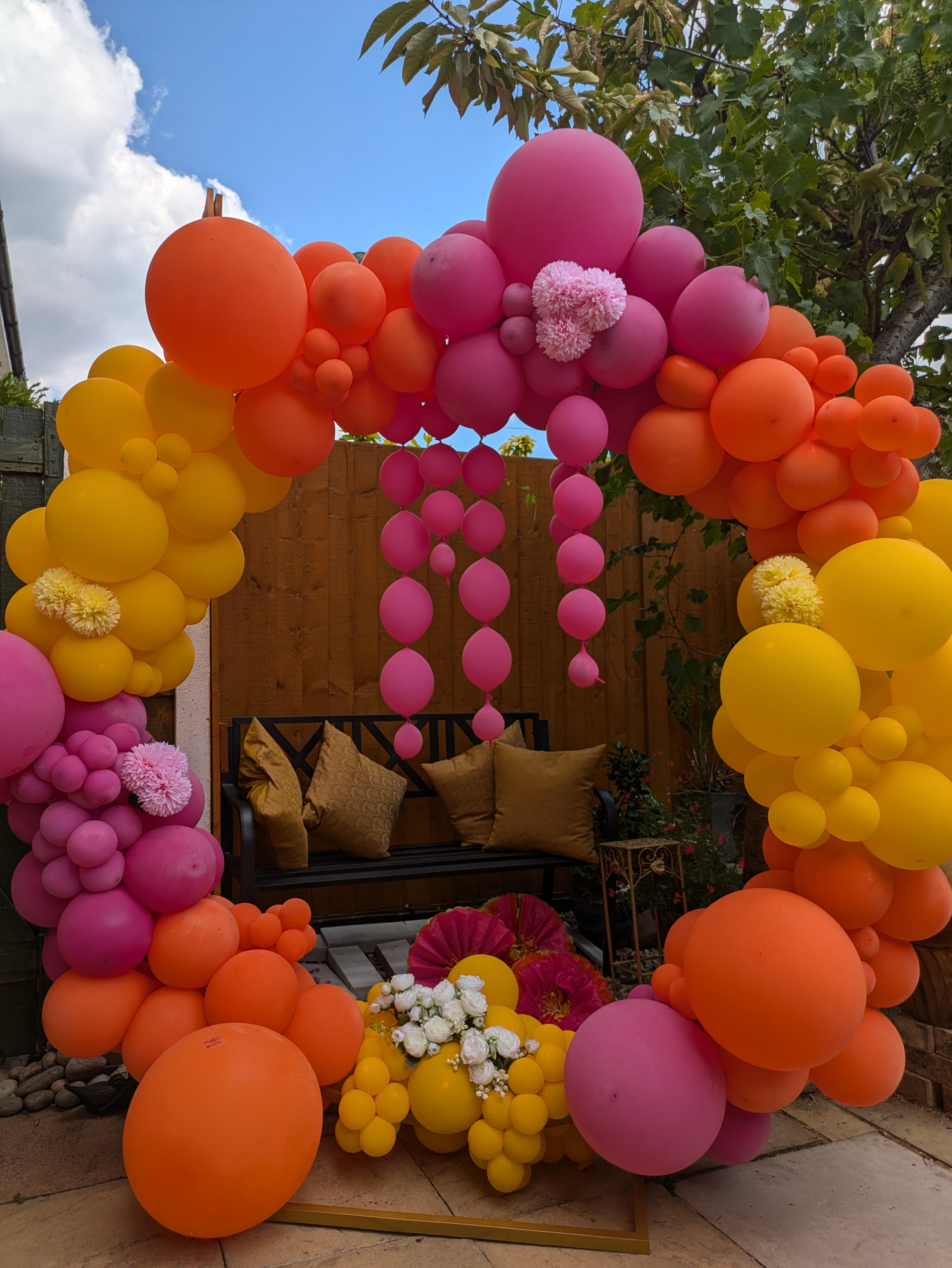 A huge ring made of orange, yellow and pink balloons of different sizes supports three hanging balloon trails