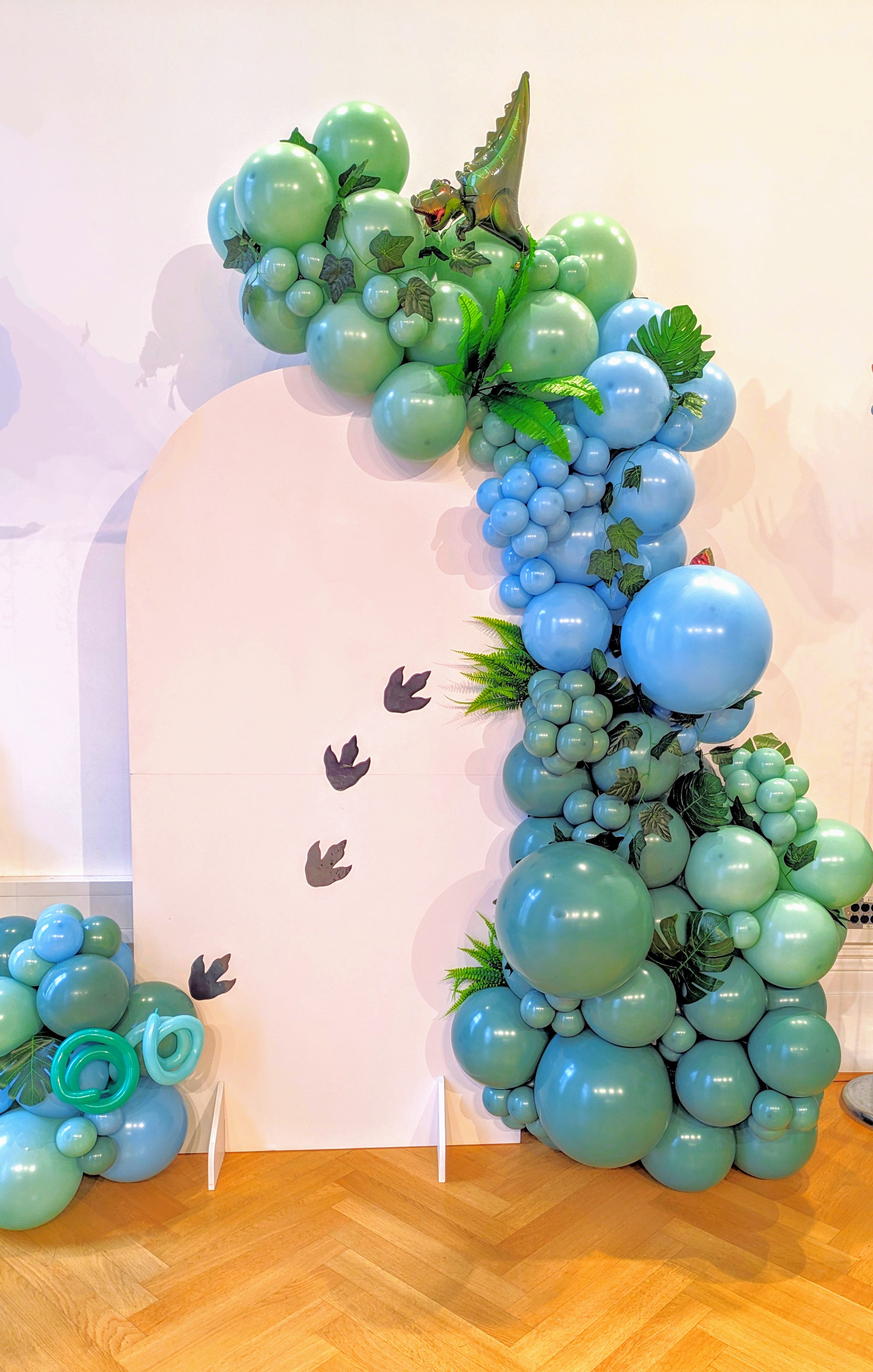 A sailboard dotted with foil dinosaur footprints is submerged under a jungle-themed balloon stack